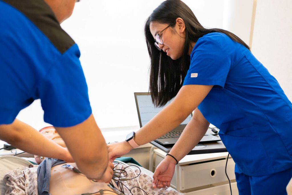 Nursing students practice using a medical mannequin in a simulation lab, focusing on patient care techniques.