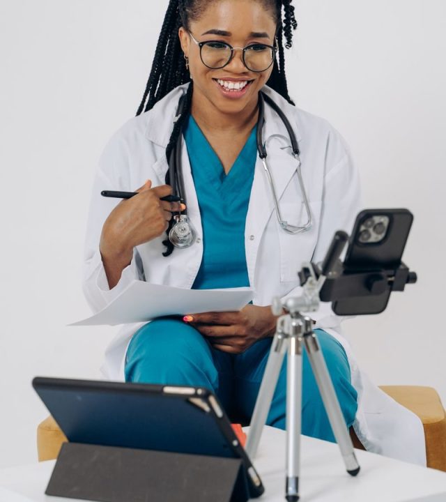 Smiling healthcare professional in scrubs using technology for an online consultation.