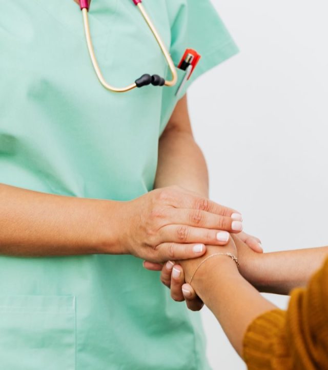 A nurse in green scrubs gently clasps a patient's hand, offering support.