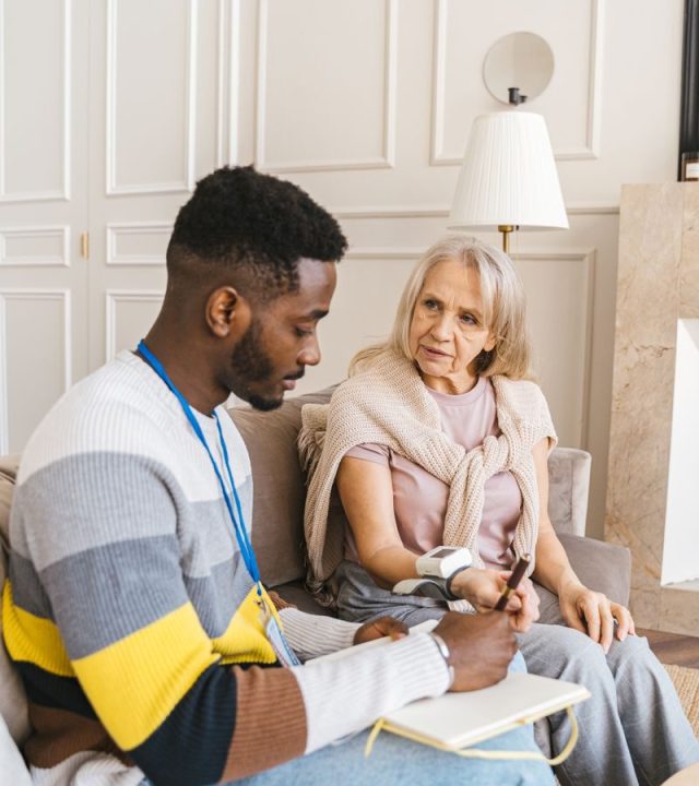 A caring volunteer assists an elderly woman in monitoring her blood pressure indoors.